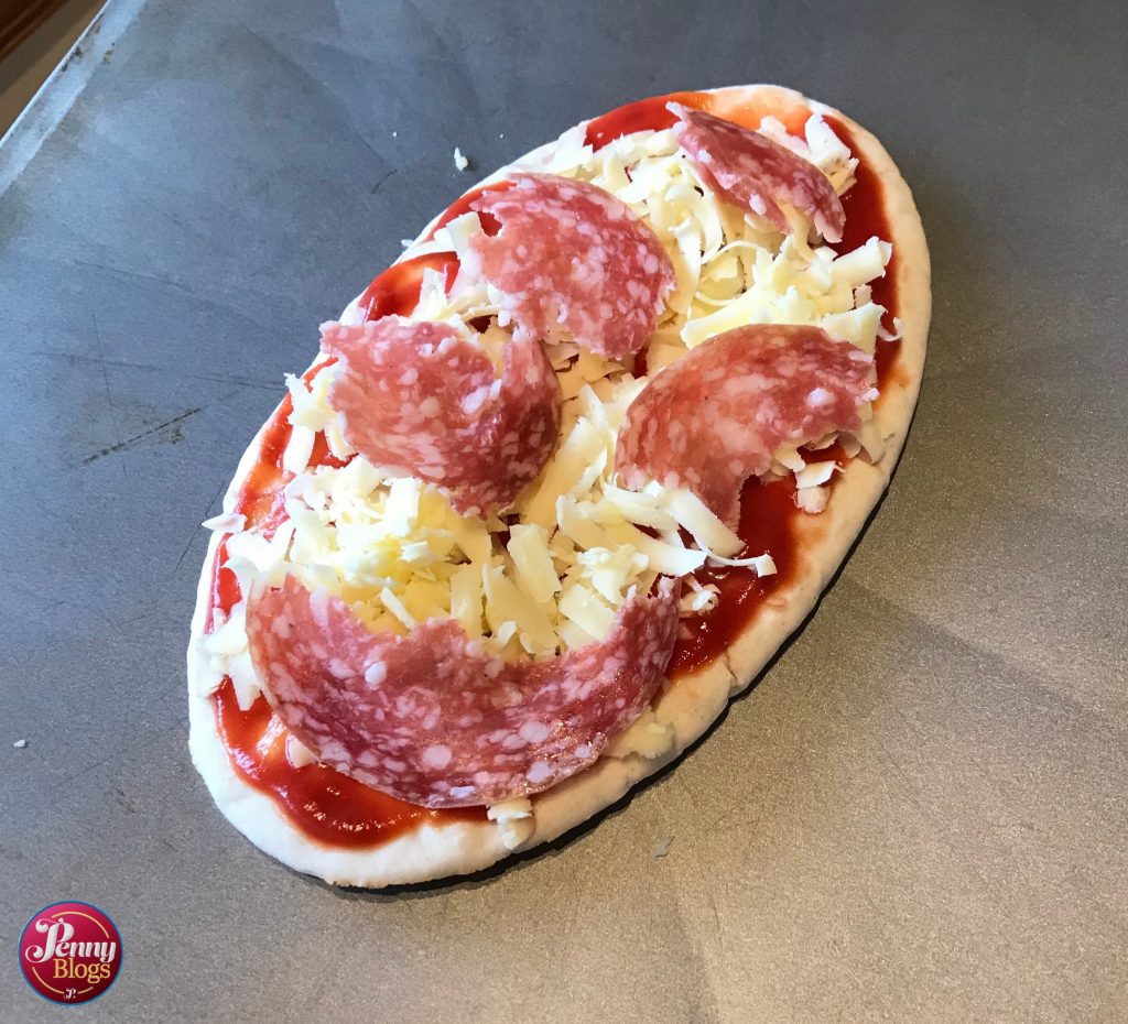 A complete pitta bread pizza with tomato, cheese na salami on it ready for the oven