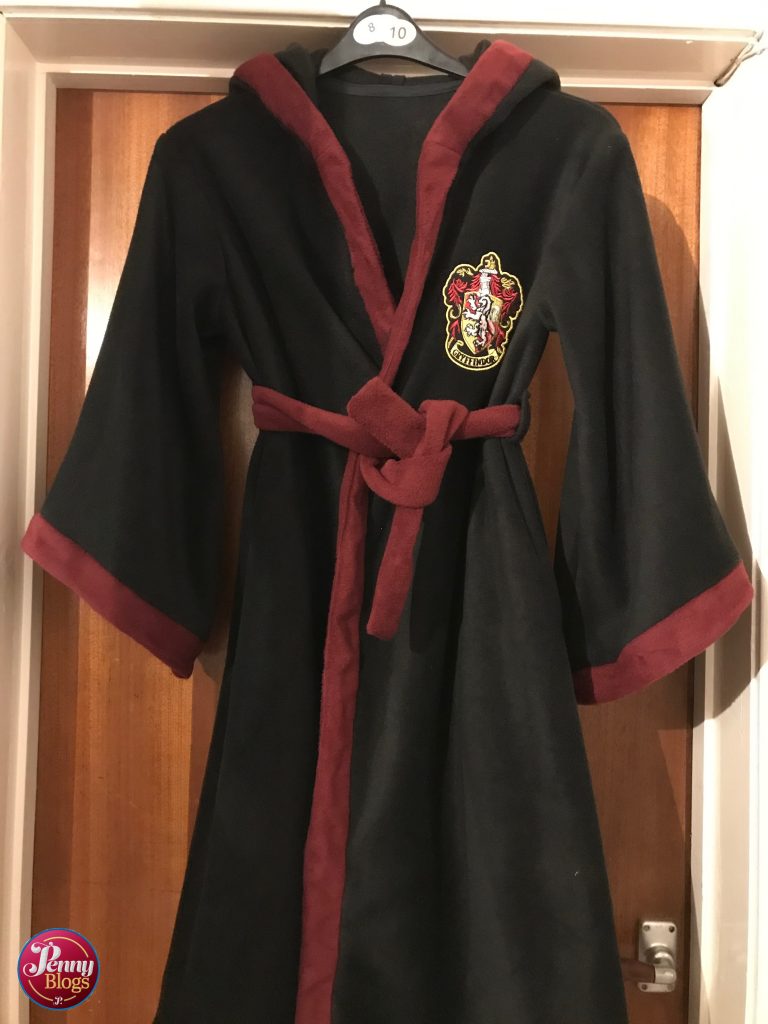 A completed Harry Potter Dressing Gown hanging on the back of a door. Mainly black in colour with a wine red trim and a Gryffindor badge on one side of the chest