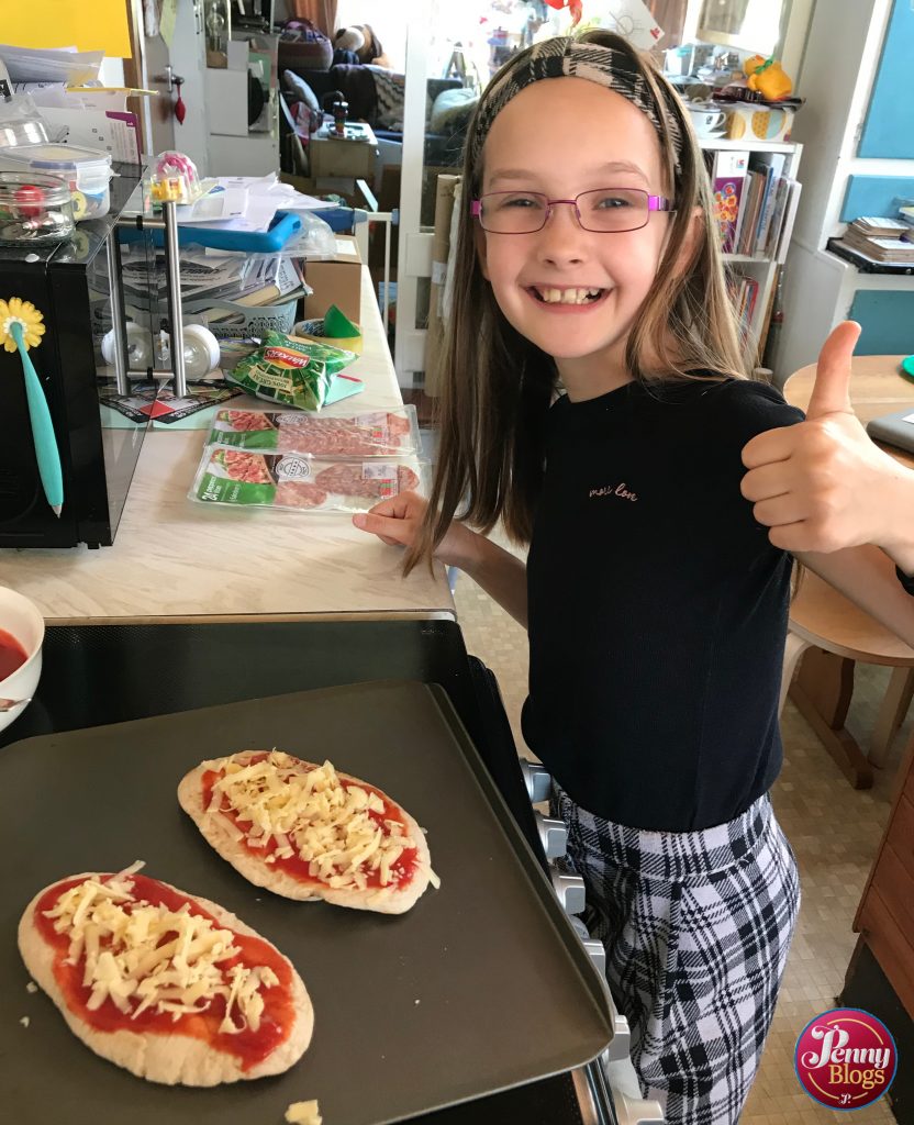 A girl showing a thumbs up next to two pitta bread pizzas ready to go into the oven