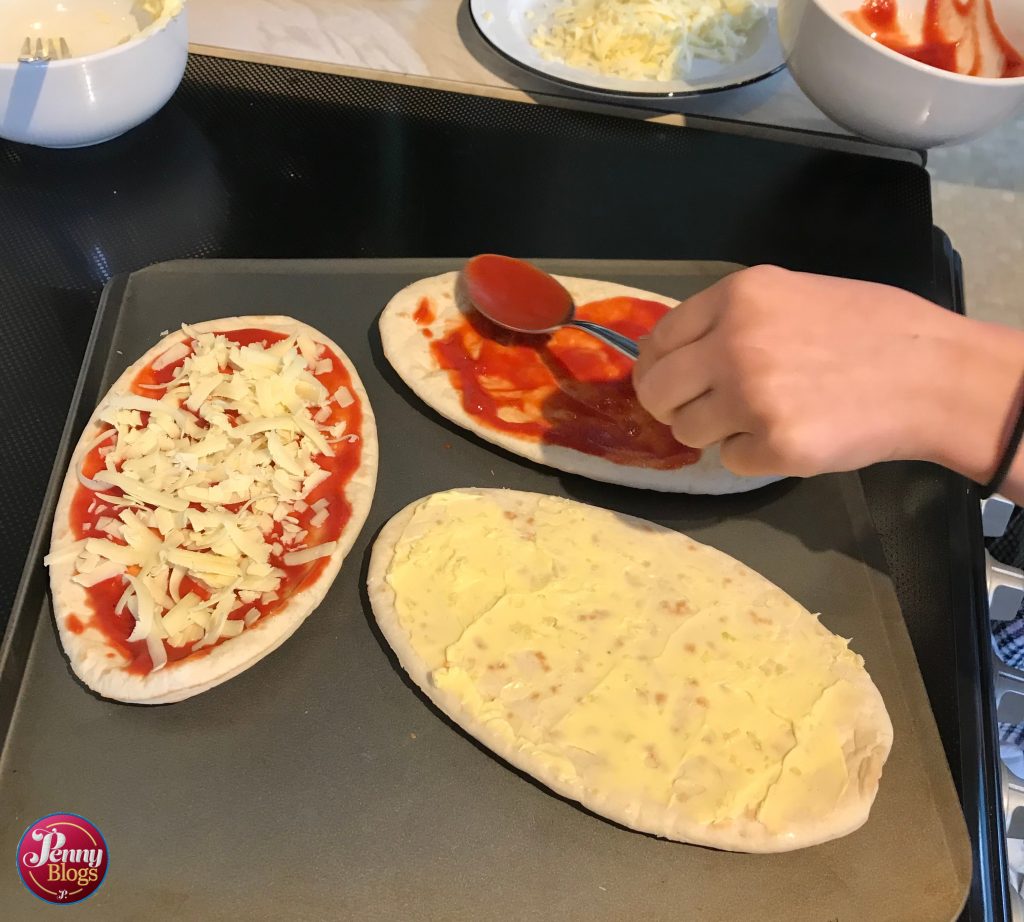 A hand spreading pasta on a pitta bread using the back of a spoon