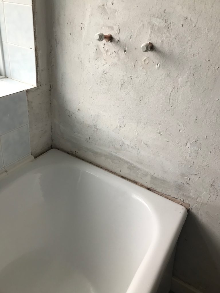 A wall with dodgy looking plastering but showing two capped off pipes sticking out of it.