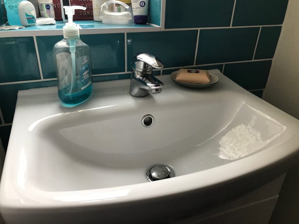 A close up of a white washbasin with petrol blue metro style tiles around it.