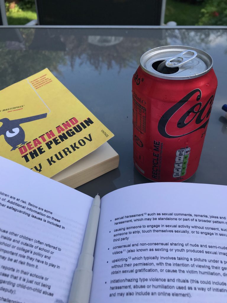 A open copy of Keeping Children Safe in education sits next to a can of coke and a copy of Death and The Penguin.